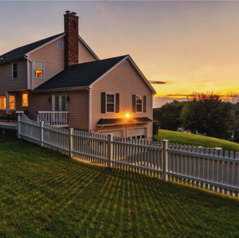 a house on a property with a white fence with a sunset in new york