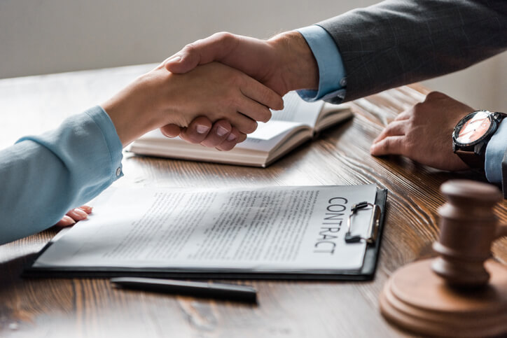 cropped shot of lawyer and client shaking hands above contract