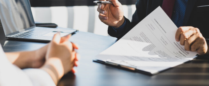 Businessman in suit in his office showing an insurance policy and pointing with a pen where the policyholder must to sign. Insurance agent presentation and consulting insurance detail to customer.