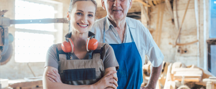 Senior master carpenter with his granddaughter in the wood workshop looking at camera