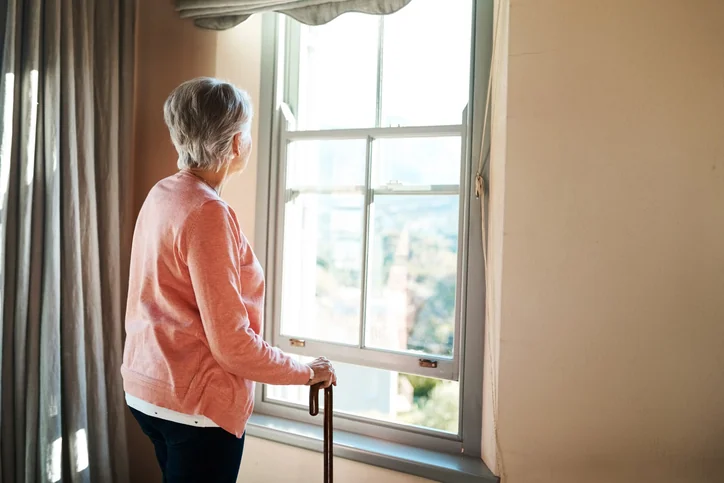 Old woman with cane looking out a window