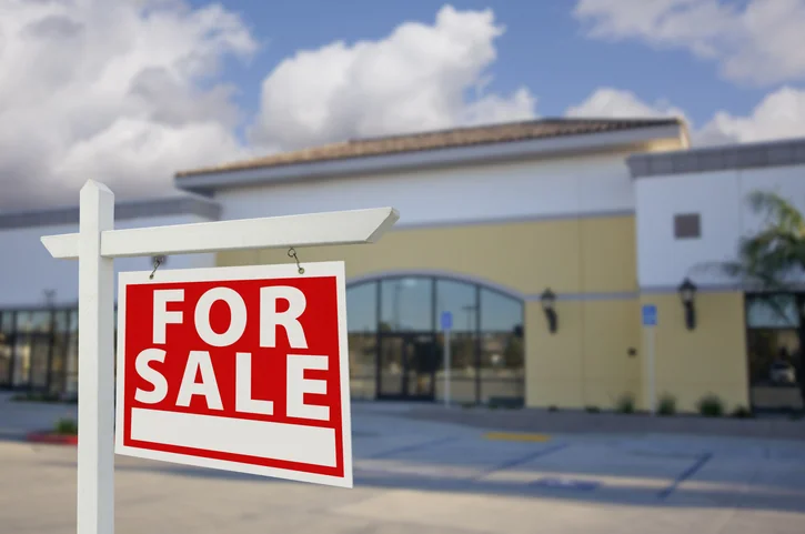 Vacant Retail Building with For Sale Real Estate Sign in Front.